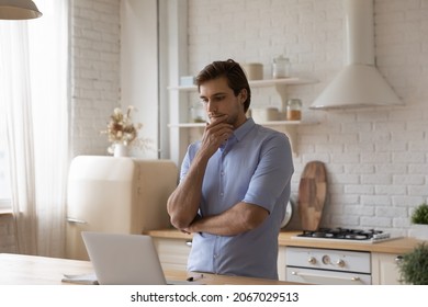 Pensive businessman standing in kitchen staring at laptop screen thinks over task looks thoughtful, work on online project, freelancing and telecommuting occupation from home, use modern tech concept - Shutterstock ID 2067029513