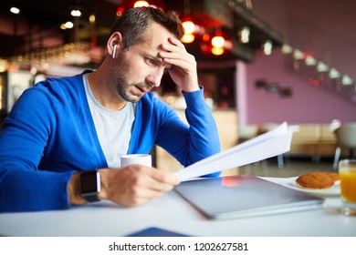Pensive businessman with wireless earphones concentrating on paperwork while working in cafe - Shutterstock ID 1202627581