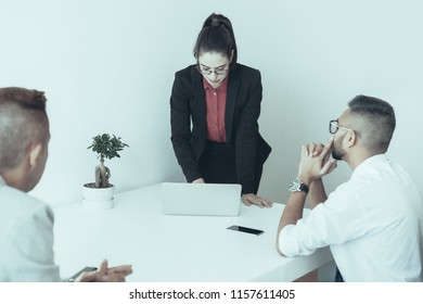 Pensive Businesswoman Preparing For Presentation And Using Laptop To Find Document While Colleagues Sitting At Table And Waiting. Staff Meeting Concept