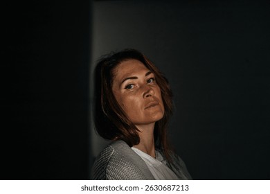 Pensive caucasian female adult in shadowy light with thoughtful expression.