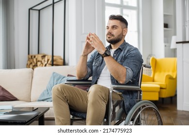 Pensive Caucasian Male With Disability Sitting In Living Room And Looking Away With Calm Face. Thoughtful Man In Wheelchair Spending Free Time Alone At Home.