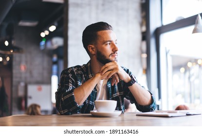 Pensive Caucasian Millennial 20 Years Old Resting In Cafeteria Thinking About Journalism During Free Time, Pondering Male Customer Dressed In Trendy Shirt Looking Away During Coffee Time In Local