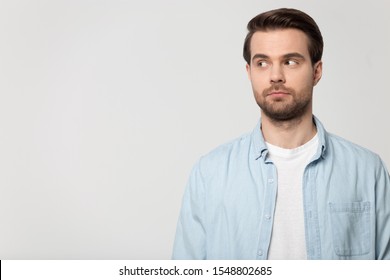 Pensive Caucasian millennial man in casual clothes isolated on grey studio background look aside at blank copy space, thoughtful guy pondering considering good sale offer, promotion discount