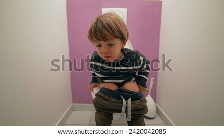 Pensive child seated at bathroom toilet. 3 year old boy doing his needs in lavatory