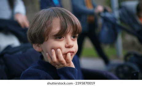 Pensive child thinking while seated on stroller with hand in chin. Young boy observing world with thoughtful expression while being carried in carriage
