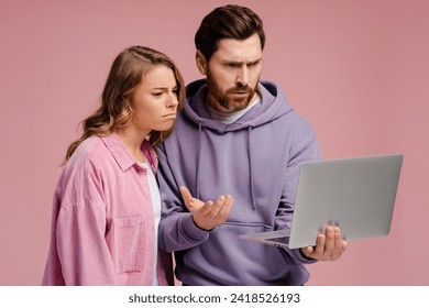 Pensive couple holding laptop computer choosing goods isolated on pink background. Stylish man and woman shopping online looking at screen. Technology concept - Powered by Shutterstock