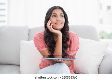 Pensive cute brunette sitting on couch holding tablet in bright living room - Shutterstock ID 160538360