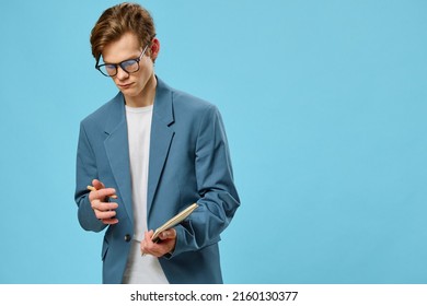 Pensive Cute Guy In A Jacket And Glasses On A Blue Background