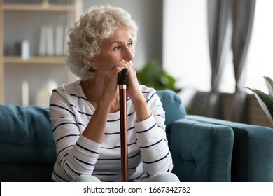 Pensive disabled old lady sit on couch in living room look in window distance thinking pondering, thoughtful mature 50s woman with walking cane lost in thoughts mourning feel loneliness solitude - Powered by Shutterstock