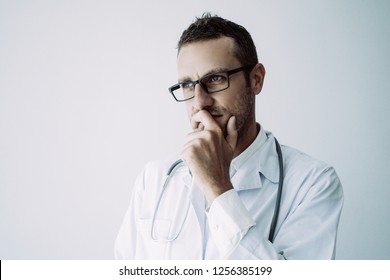 Pensive Doctor In Glasses Reflecting On Patient Treatment. Focused Practitioner Leaning Head On Hand, Covering Mouth With Fist. Decision Making And Medicine Concept