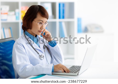 Pensive doctor reading some information on the laptop screen