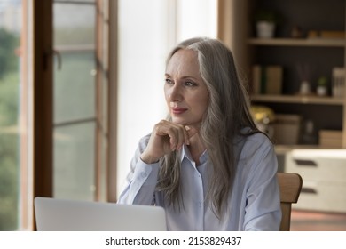 Pensive Dreamy Older 60s Business Lady Sitting At Laptop Computer, Looking At Window Away, Planning Work Tasks, Making Decision, Thinking Over Offer. Mature Employee, Student Portrait