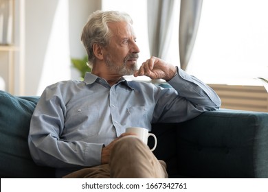 Pensive elderly 60s man sit relax on couch in living room drinking tea look in window distance thinking, thoughtful mature 50s husband rest on sofa at home feel sad pondering considering future - Powered by Shutterstock