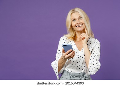 Pensive Elderly Gray-haired Blonde Woman Lady 40s 50s Years Old In White Dotted Blouse Using Mobile Phone Typing Sms Message Put Hand Prop Up On Chin Isolated On Violet Background Studio Portrait