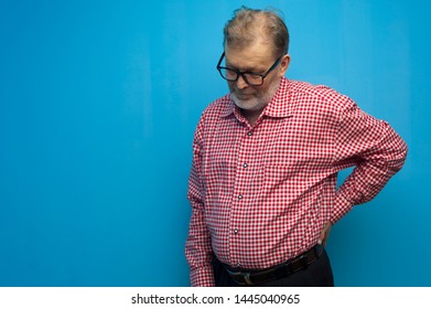 Pensive Elderly Man In A Red Shirt And Glasses Posing On A Blue Background. The Concept Of Single Older Men. Advertising Space