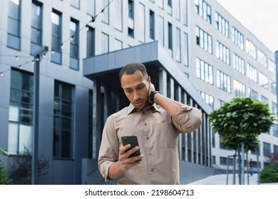 Pensive and excited african american worker outside office building reading bad news, man holding phone.