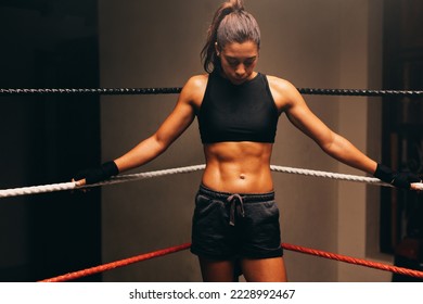 Pensive female boxer standing in one corner of a boxing ring without gloves. Sporty young woman having a training session in a boxing gym. - Powered by Shutterstock