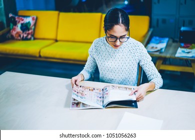 Pensive Female Editor Of Magazine Reading Issue For Checking Articles And Publication While Sitting At Table ,concentrated Woman Choosing Items In Paper Catalogue For Buying Furniture In Office