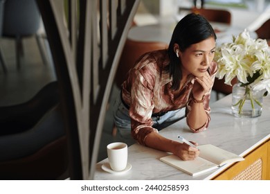 Pensive female entrepreneur listening to music and filling gratitude journal - Powered by Shutterstock