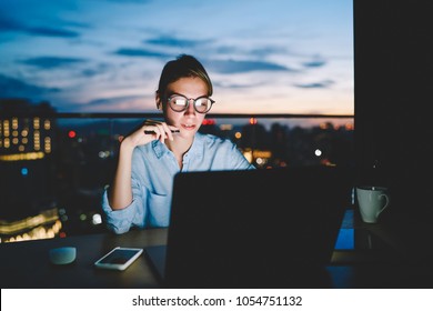 Pensive female freelancer working on publication for share on web page sitting with laptop at desktop late, woman owner of online business staying overtime with distance job reading news on netbook