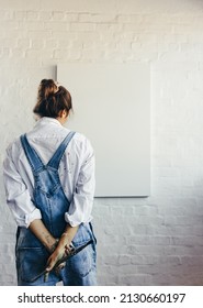 Pensive female painter looking at a blank canvas while holding a paintbrush in her art studio. Rearview of an imaginative young artist contemplating creative ideas for her new project. - Shutterstock ID 2130660197