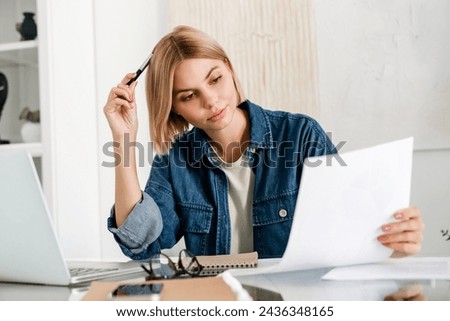 Pensive freelancer doing paperwork working on the laptop. Caucasian young woman holding report, mortgage document, project, solving dealing with problem