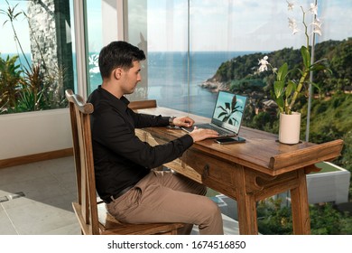 Pensive Freelancer Man Working At A Computer In The Hotel Of His Luxurious Room With Wood Finishes And Sea Views. The Work Is Not Tied To The Place Of Residence. Work In Any Place. Freelance.