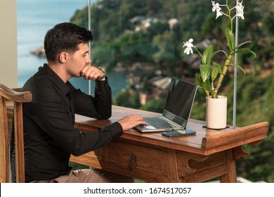 Pensive Freelancer Man Working At A Computer In The Hotel Of His Luxurious Room With Wood Finishes And Sea Views. The Work Is Not Tied To The Place Of Residence. Work In Any Place. Freelance.