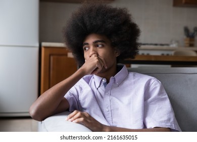 Pensive Frustrated Teenage African Guy With Fuzzy Curly Hair Sitting On Couch At Home, Looking Away, Thinking Over Troubles, Bad News, Feeling Bored, Sad, Depressed. Youth, Negative Emotions Concept