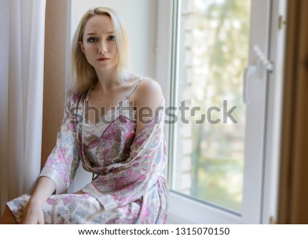 Pensive girl in bathrobe sitting on the windowsill. Natural light.