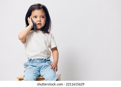 Pensive Girl Of Preschool Age Stands On A Light Background With A Phone