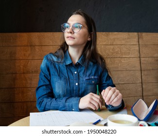 A Pensive Girl  In Round Glasses Sits In A Cafe And Looks To The Side, She Fills Out A Lifestyle Schedule Drawn By Her With Felt Tip Pens, Portrait, A Business Photo Session