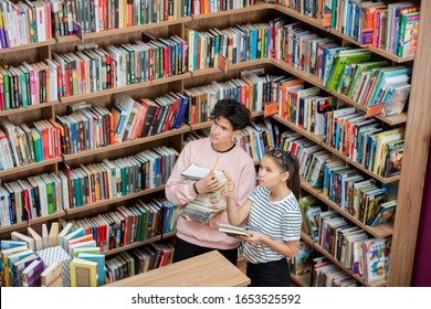 Pensive guy and his clever classmate looking at large bookshelf in college library while the girl pointing at one of books