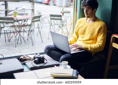 Pensive Handsome Male Blogger Updating His Profile In Social Networks With Retro Photos Sharing With Followers Multimedia Files Sitting In Coffee Shop With Equipment And Laptop Computer With Wifi