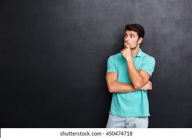 Pensive handsome young man standing with hands folded and thinking over blackboard background - Powered by Shutterstock