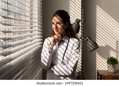 Pensive happy female doctor in white medical uniform look in window distance thinking or planning. Smiling woman nurse ponder or dream in hospital clinic, make decision. Vision, medicine concept.