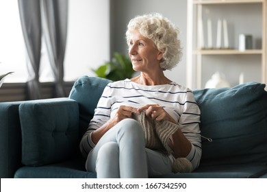 Pensive Happy Mature Old Woman Sit Relax On Couch At Home Do Knitting During Home Weekend, Smiling Elderly Grandmother Dreaming Thinking Looking In Distance Engaged In Favorite Hobby In Living Room