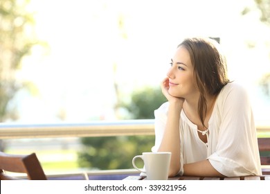 Pensive happy woman remembering looking at side sitting in a bar or home terrace