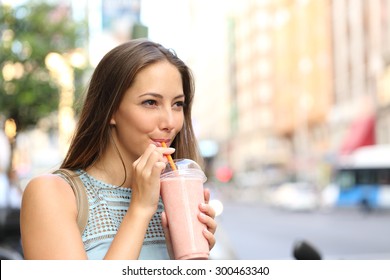 Pensive happy woman sipping a milkshake in the street  - Powered by Shutterstock