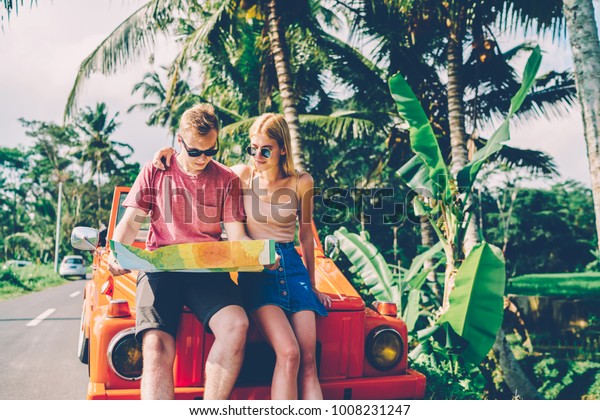 Pensive hipster couple making car stop for
checking direction and location during roadtrip, male and female
friends discussing route for getting to destination standing near
rental automobile