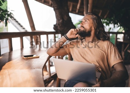 Pensive hipster guy with laptop technology thinking about remote working using 4g wireless internet at terrace, contemplative male programmer with digital netbook thoughtful looking away outdoors