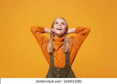 Pensive little blonde kid girl 12-13 years old in turtleneck, jumpsuit isolated on orange yellow wall background. Childhood lifestyle concept. Mock up copy space. Looking up with hands behind head - Shutterstock ID 1634511082