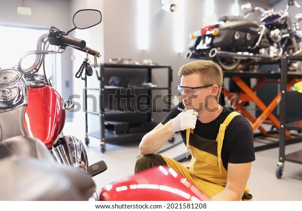 Pensive locksmith inspects technical condition\
of motorcycle in\
workshop