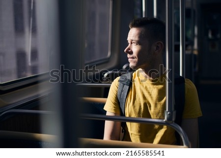 Pensive lonely man looking out of window of train. Solo traveler in public transportation on sunny day.
