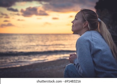 Pensive lonely smiling woman looking with hope into horizon during sunset at beach