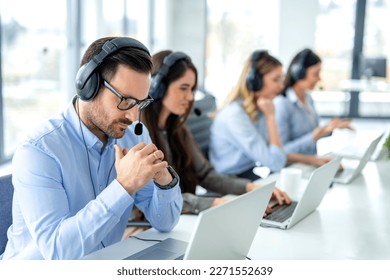 Pensive male customer service operator listening to customer over headset and thinking about appropriate solutions for client issues at call center. Helpdesk worker team concept. - Shutterstock ID 2271552639