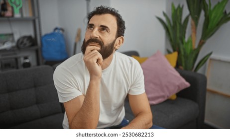 Pensive man with beard in white shirt sits indoors contemplating in a cozy living room. - Powered by Shutterstock