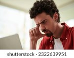 Pensive man checking programming code for errors when working on laptop from home