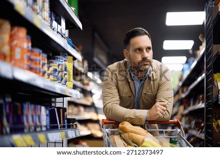 Pensive man feeling worried about increase of prices while shopping groceries in supermarket. 