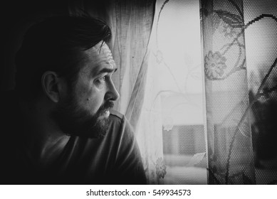 Pensive man looking through the window. Black and white portrait